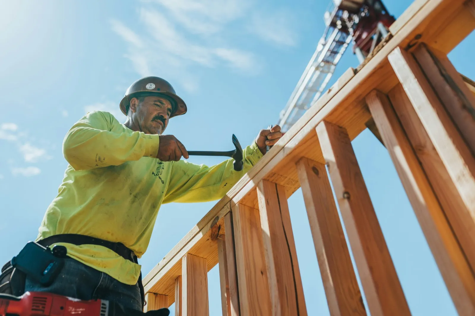 Builder nailing off framing against a blue sky